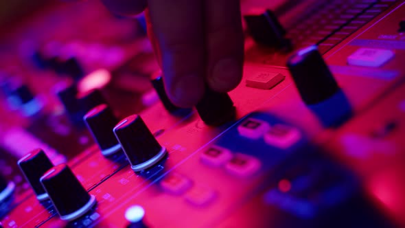 Closeup of DJs Hands Twisting Knobs on Mixing Console Adjusting Volume of Dubstep in Nightclub Disco