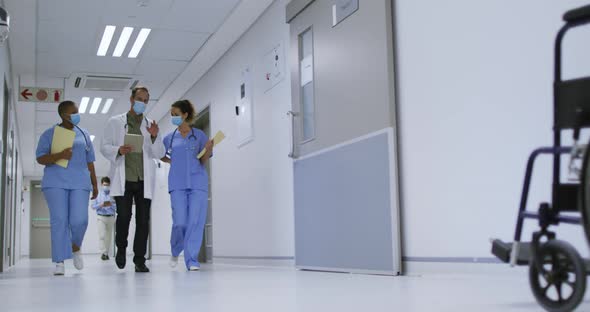 Diverse group of male and female doctors wearing face masks walking in hospital corridor talking