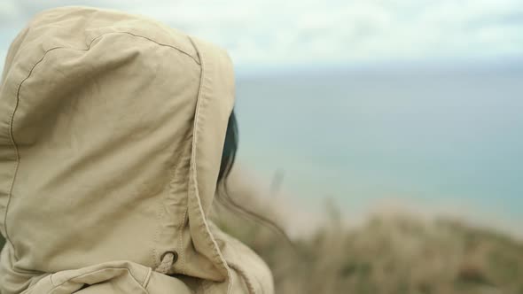 A Girl in a Hood Waves Her Hand and Sends Air Kisses to the Camera By the Sea