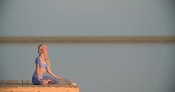 Woman is Sitting on the Wooden Pier of the Lake and Meditating During Sunset