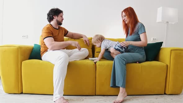 Family Sitting on Yellow Couch  the Mother Puts the Baby Down on the Floor