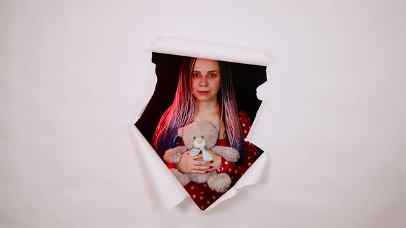 Young Woman with Teddy Bear Looking Out of Hole of White Background