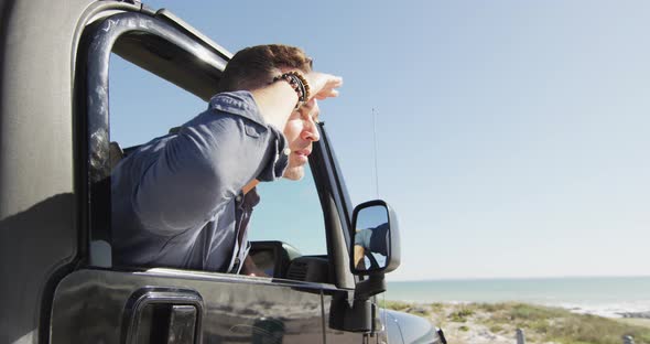 Happy caucasian man in car admiring the view on sunny day at the beach