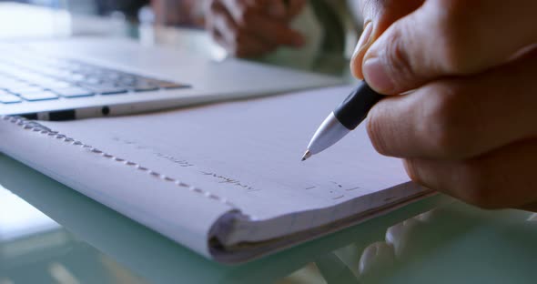 Man writing on notepad while using laptop at home 4k