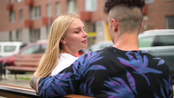 A young couple sits on a bench in the city and communicates, kisses