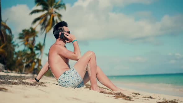 Man Talking On Cellphone.Man Sitting And Talking On Smartphone On Vacation Lounge Sea.Tropical Beach
