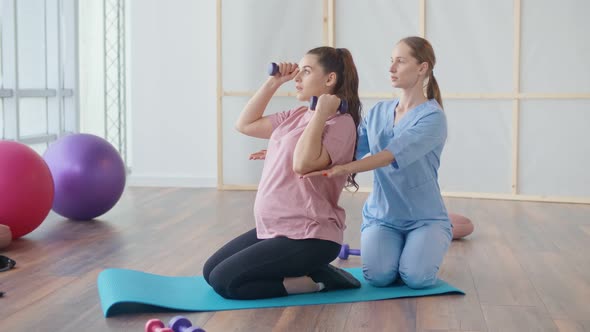 A Young Pregnant Woman is Doing Exercises with a Health Worker in a Clinic