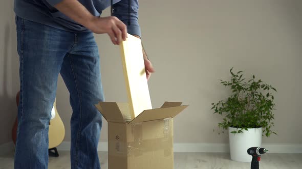 Man Unpacks Cardboard Box Takes Out Pieces of Wooden Furniture