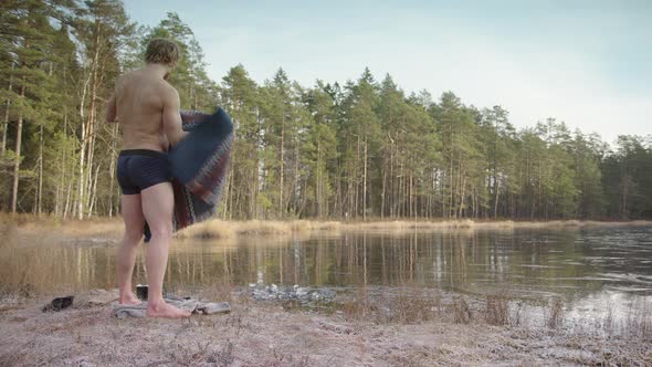 ZOOM IN - A fit muscular ice bather res his poncho and prepares to enter the frozen lake