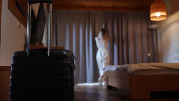 Black Suitcase with Baggage and Blurred Caucasian Young Woman Opening Curtains at Background in