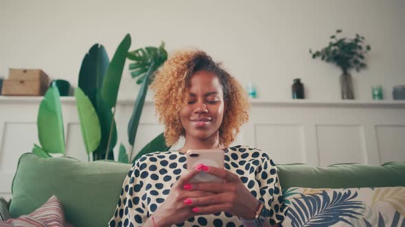 Relaxed Woman Sitting at Home on Sofa and Enjoying Funny Online Chat