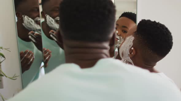 African american father and son putting shaving cream on their faces and laughing together