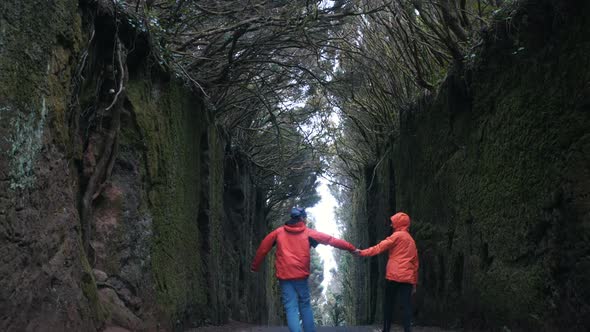 Young Optimistic Couple Holding Hands Walks and Turns Around on a Tunnel Road Between Rocks Covered