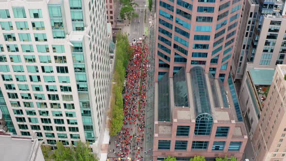 Huge crowd of protesters moving below, pull back tilt aerial in a major city downtown