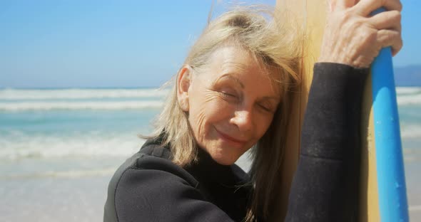 Front view of active senior Caucasian female surfer standing with surfboard on the beach 4k