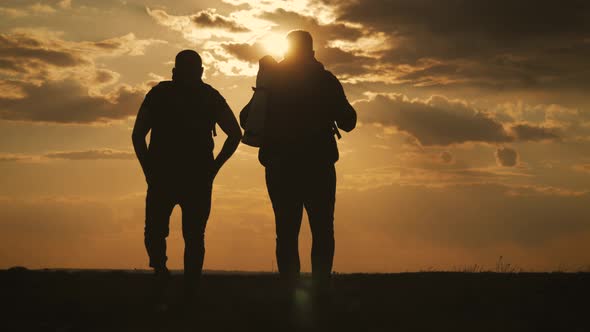 Two Friend Tourists Walk Along the Lake at Sunset. Traveling with Backpacks in Warm Weather in