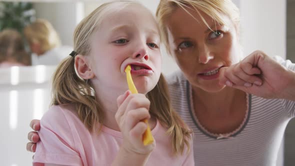 Side view of Caucasian girl brushing her teeth and advising by her mother