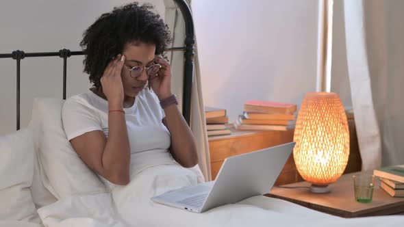 African Woman with Laptop Having Headache in Bed