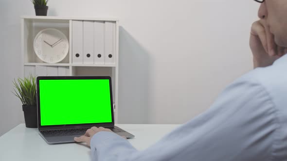 A Man Using a Laptop with a Green Screen