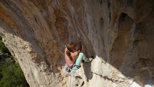 Young Powerful Athletic Man Rock Climber with Long Hair Climbing on Overhanging Cliff