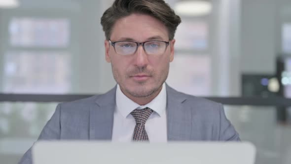 Close Up of Middle Aged Businessman with Laptop Looking at Camera