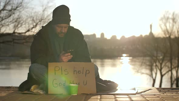 Homeless Man Using Mobile Phone While Begging