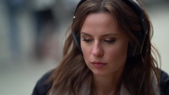 Woman Is Enjoying Favorite Music in Headphones and Hot Coffee or Tea in Cafeteria, Sitting on Open