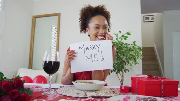 Mixed race woman on a valentines date video call, holding marry me proposal sign