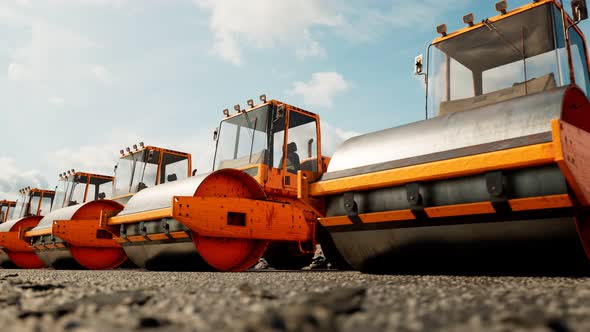 An endless row of yellow big road rollers standing in the row.  Heavy machines.