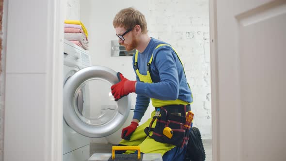 Young Handsome Repairman in Uniform Fixing Broken Washer