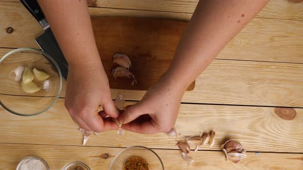 Top view of a woman's hands on a cutting board crushing garlic cloves with a large knife
