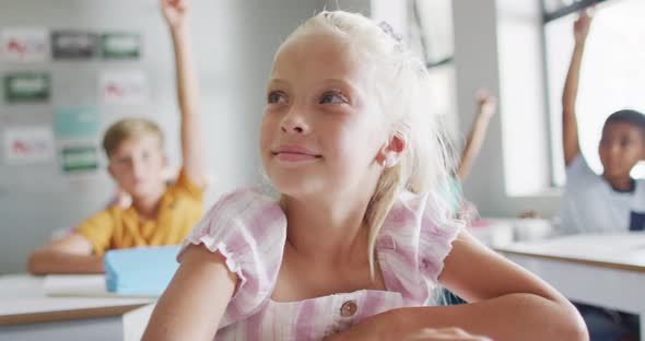 Video of happy caucasian girl raising hand during lesson in classsroom