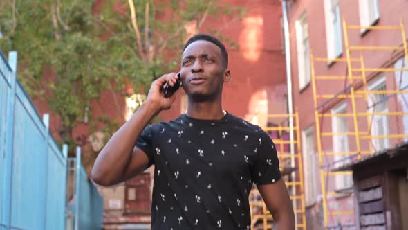 A young smiling black guy is walking down the street and talking on the phone
