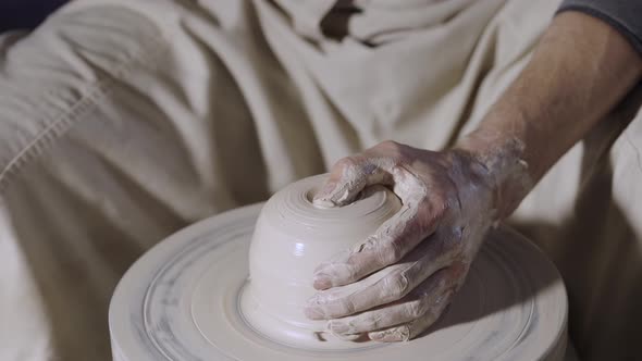 The Potter's Male Hands Shape and Sculpt the Soft White Clay Pot Spinning on a Potter's Wheel in a