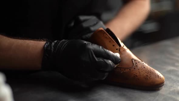 Close-up of unrecognizable shoemaker in black latex gloves polishing old light brown leather shoes