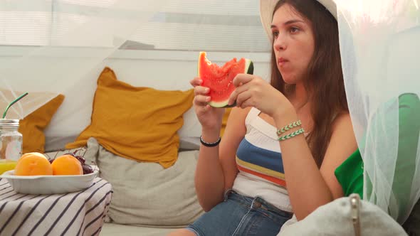 Young woman eating fresh watermelon in backyard tent