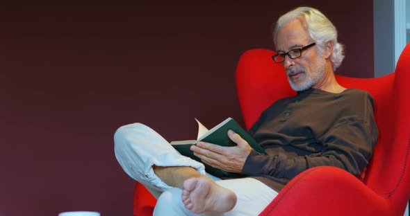 Senior man reading a book in living room 4k