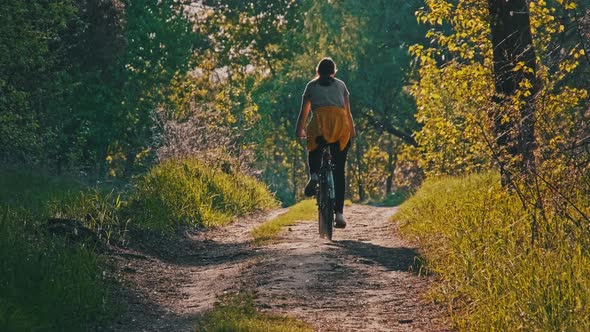 Young Woman on Bicycle Rides Along Green Forest Path in Summer Day Slow Motion