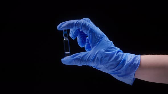 Closeup of Hand Wearing Blue Medical Glove Holding Ampoule with Vaccine Against Coronavirus