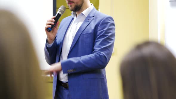 Man in blue suit is speaking in the conference hall gesticulating with his hand. 