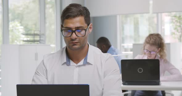 Medium Shot of Indian Businessman Working on Laptop Near Colleagues in Office