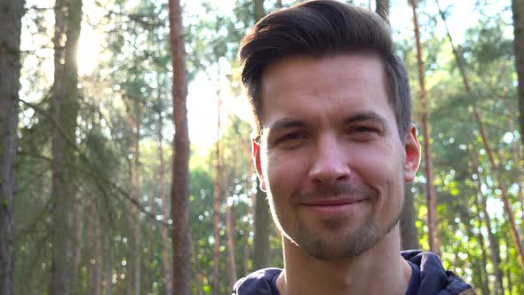 A Young Backpacker Smiles at the Camera in a Forest - Face Closeup From Below