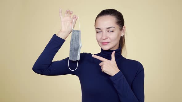 Young Woman Holds Medical Mask in Her Hands and Shows Gesture Thumbs Up