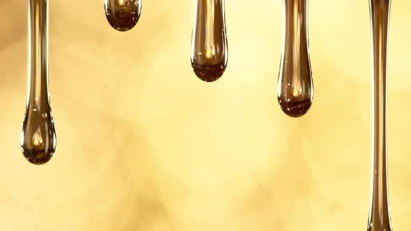 Super Slow Motion Macro Shot of Dripping Oil on Golden Background at 1000 Fps