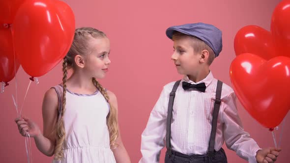 Couple of Little Kids in Love, Holding Red Heart Balloons, Smiling Into Camera