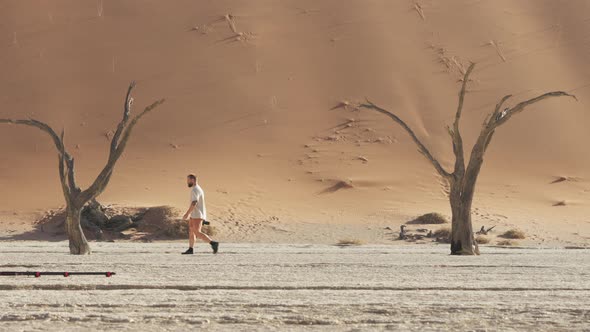 Man Walking At Deadvlei With Dead Camelthorn Trees And High Red Dunes In The Background. - wide shot