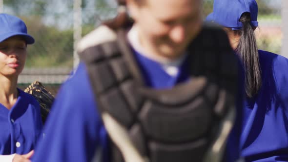 Happy diverse group of female baseball players smiling and banging gloves after game