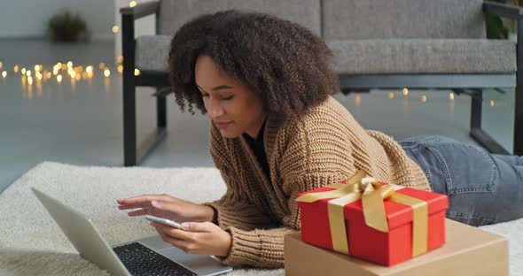 Happy African American Woman Ethnic Girl with Phone and Laptop Lying on Floor of House in Living