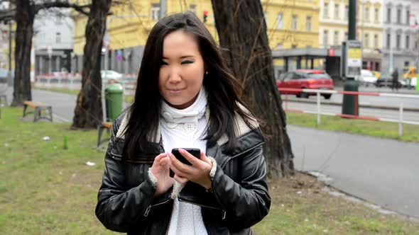 Young Attractive Asian Woman Works on Smartphone and Smiles - Urban Street with Car - City