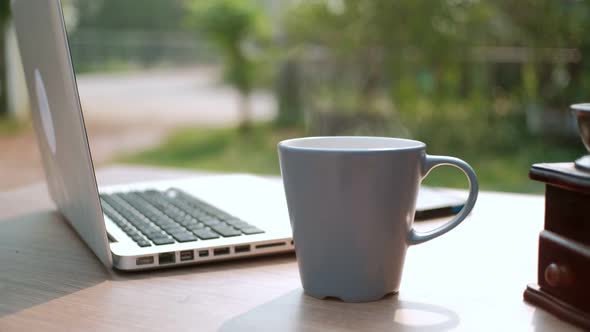 Close up Cup of coffee, coffee with smoke on desk table with laptop computer background in morning.